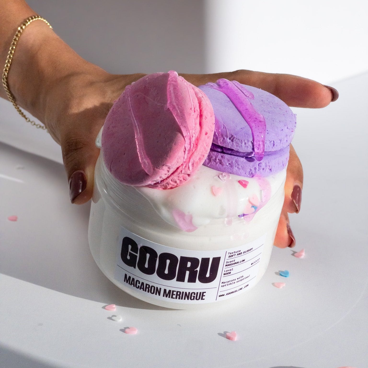 A hand carrying a jar of Macaron Meringue white slime with two pink and purple clay Macarons. 