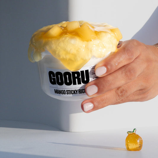 A hand carrying a jar of Mango Sticky Rice slime with white base and mango colored clear slime and a mango charm on the side