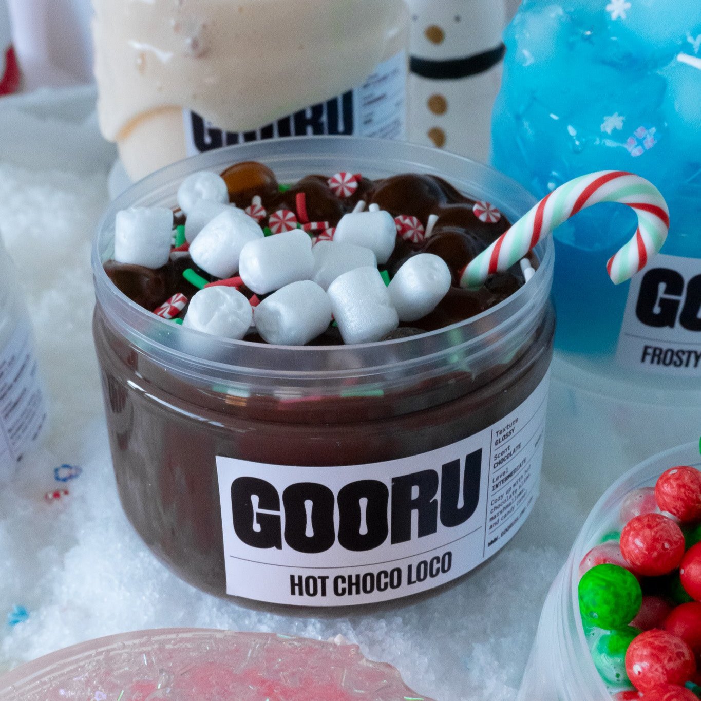 A group display featuring the Hot Choco Loco slime jar surrounded by other festive slime jars, including Holiday Bake Shop and Frosty Wonderland. The glossy chocolate base and holiday-themed toppings stand out with cozy holiday charm.