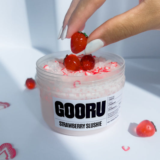 Product shot of a hand placing a strawberry charm int Strawberry Slushi Slime, designed and manufactured  by Gooru Slime, Dubai, UAE