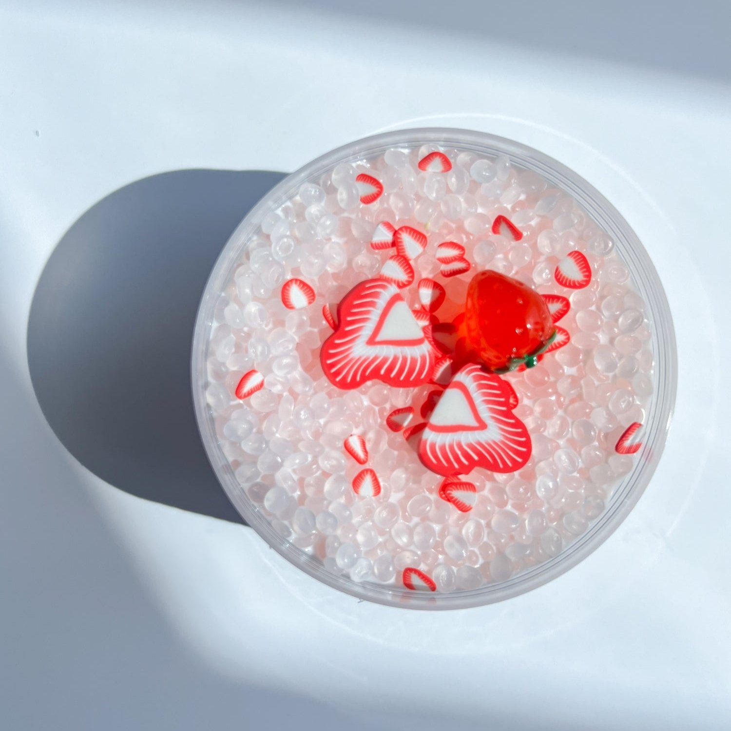 Top view product shot of Strawberry Slushi Slime, with red strawberry charmes, designed and manufactured  by Gooru Slime, Dubai, UAE