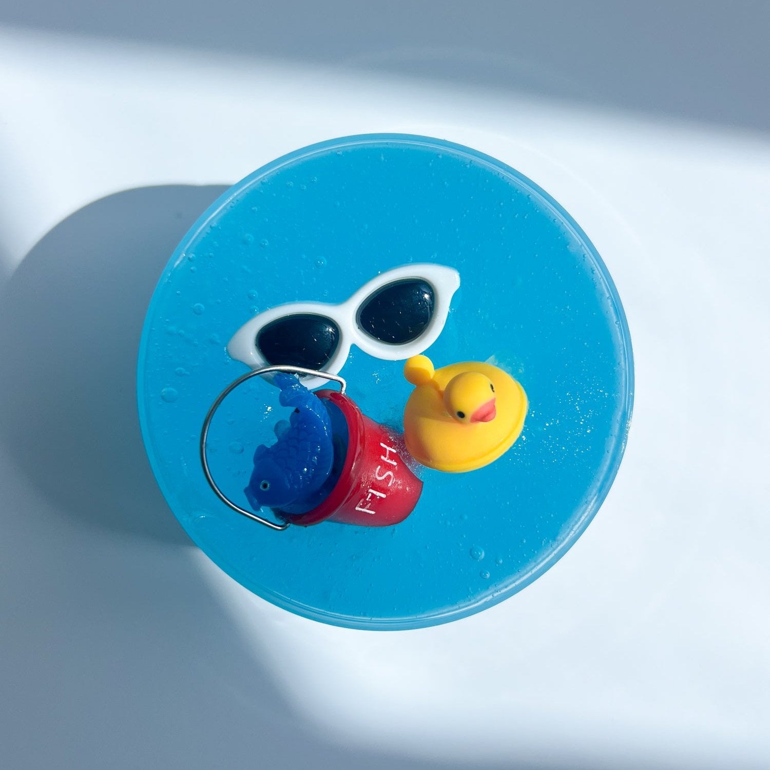 Top view product shot of Beach day Slime, with beach bucket and sunglasses charms on top, designed and manufactured  by Gooru Slime, Dubai, UAE