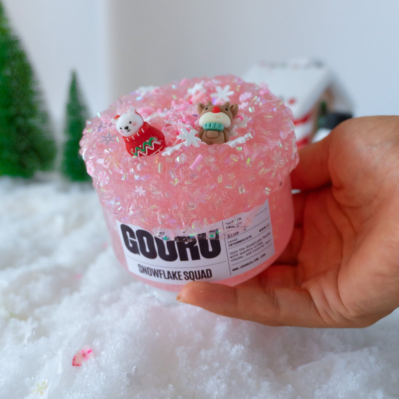 A jar of Snowflake Squad slime with a pink crunchy texture, adorned with snowflake charms and holiday figurines. The lid features a polar bear in a festive sweater and a reindeer charm, creating a cheerful winter vibe.